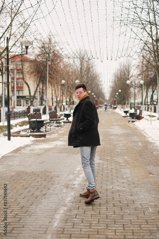 A young man turning around leaves in the city view in the city goes along the avenue. hipster man in winter city