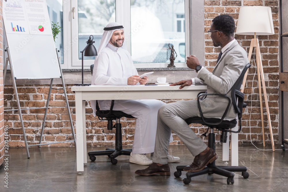 Multiethnic businessmen talking and smiling in modern office Multiethnic businessmen talking and smiling in modern office