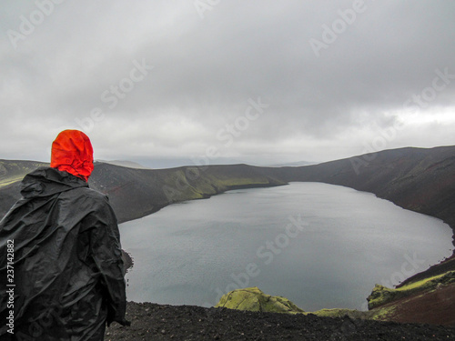 Hiker adventurer hiking in raincoat back standing outdoor looking crater lake in Laugaveur trek in stunning nature landscape, Iceland