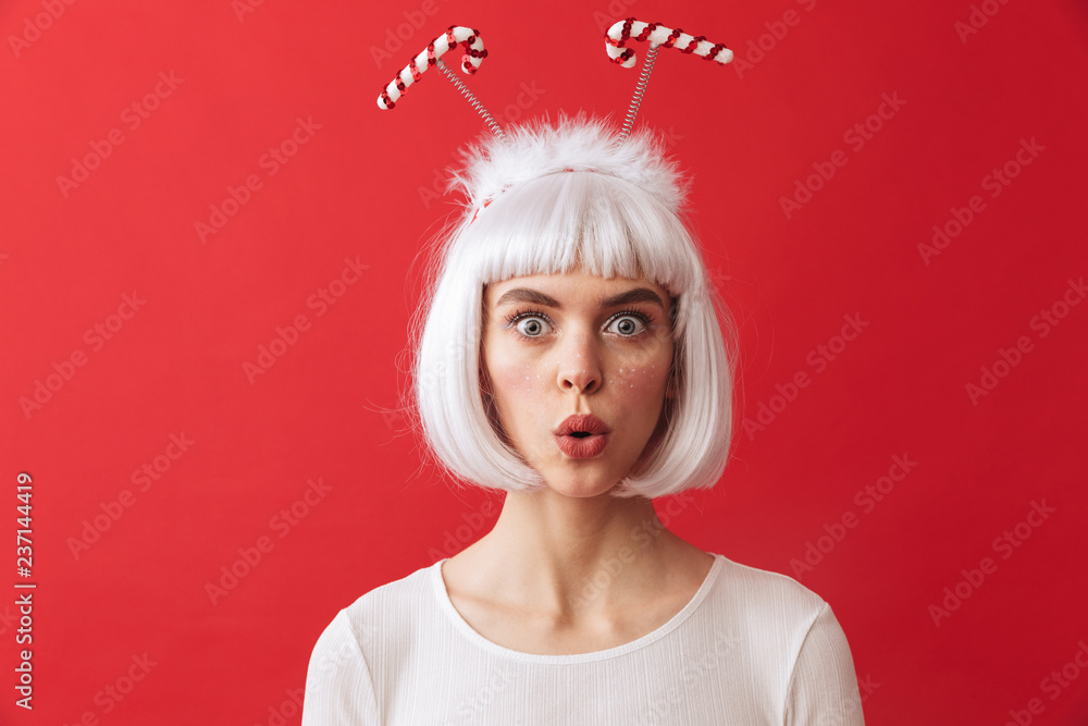 Shocked excited young woman wearing christmas carnival costume over red wall.