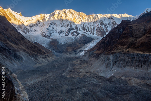 Horizontal photo of Annapurna 1 and its glacier morraine during sunrise (golden hour) against blue sky, Himalayas