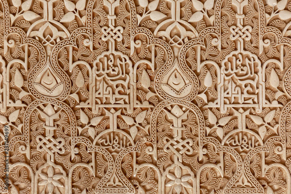 The detailed and intricate geometric patterns and Islamic calligraphy of a wall carving at the famous Alhambra palace- fortress in Granada, Spain