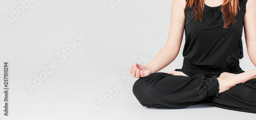 Young brunette slim woman in black sitting in Lotus position in yoga isolated on gray background, banner
