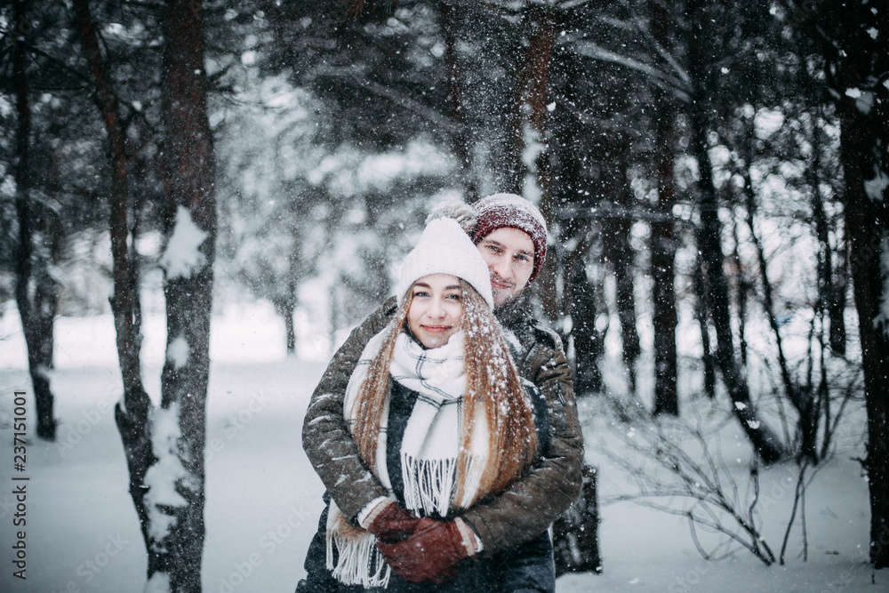 young couple in love are walking in the snowy winter forest. Positive beautiful lovers in clothes for the cold time. young couple in love are walking in the snowy winter forest. Positive beautiful lovers in clothes for the cold time.
