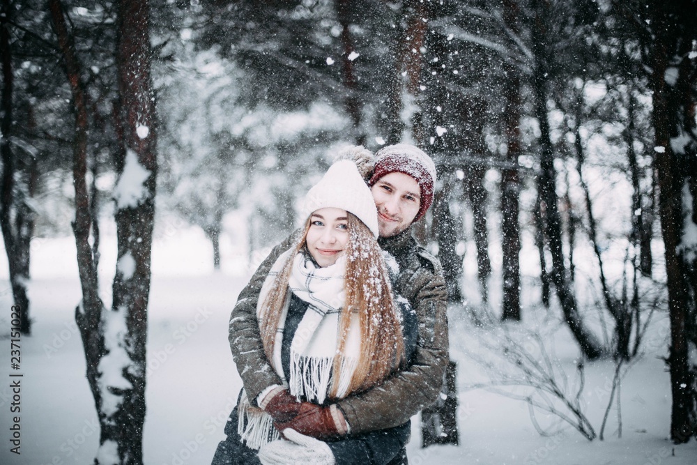  young couple in love are walking in the snowy winter forest. Positive beautiful lovers in clothes for the cold time.