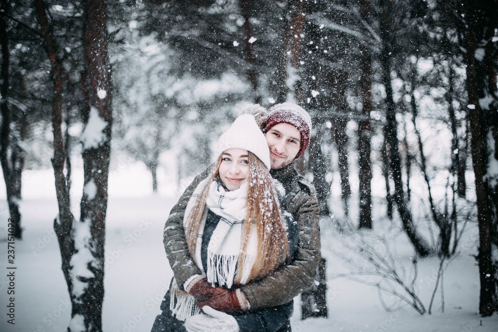 young couple in love are walking in the snowy winter forest. Positive beautiful lovers in clothes for the cold time. young couple in love are walking in the snowy winter forest. Positive beautiful lovers in clothes for the cold time.