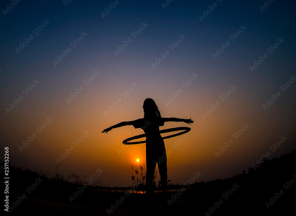 silhouette of the girl playing hula hoop in sunset background