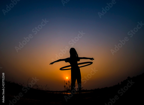 silhouette of the girl playing hula hoop in sunset background