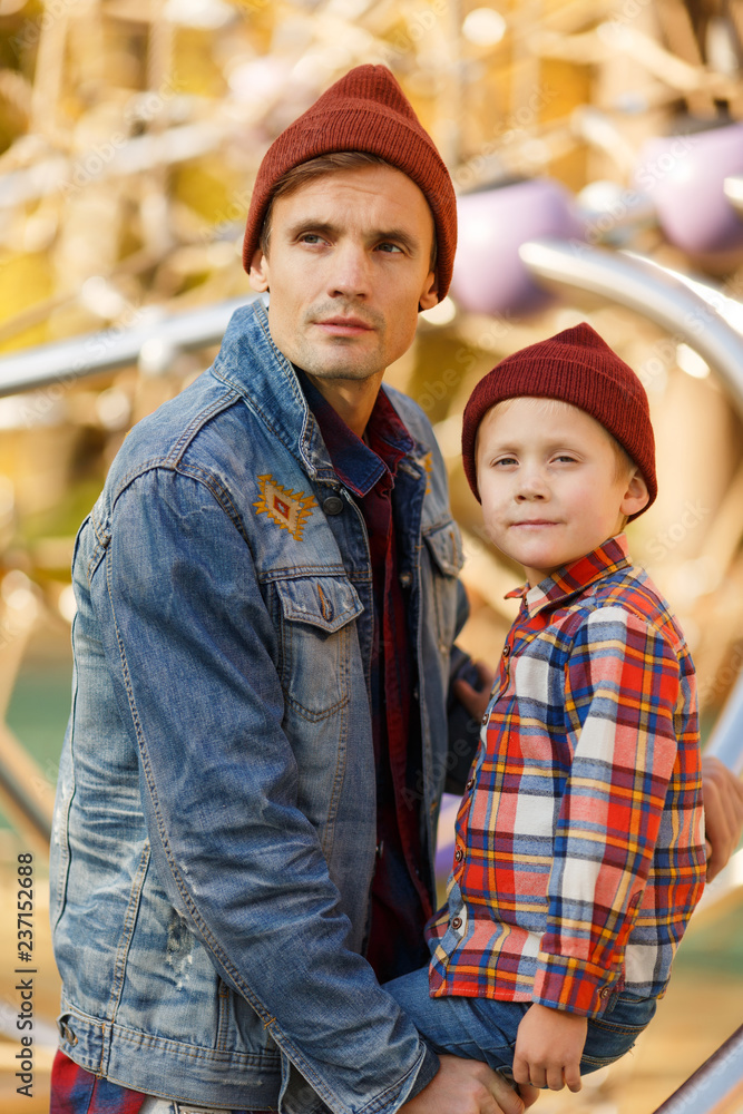 Fototapeta premium Image of young brunet with his son near iron structure in autumn park