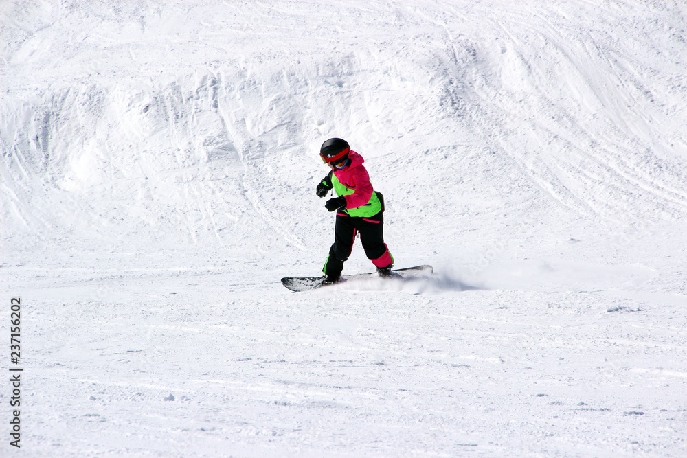 girl in a colorful suit is on a snowboard rides with mountains