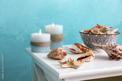 Different sea shells with burning candles on light table near color wall