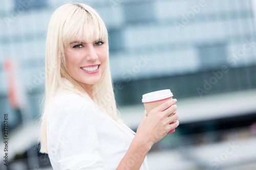 Junge Gesch  ftsfrau vor Stadtkulisse mit Kaffeebecher in der Hand