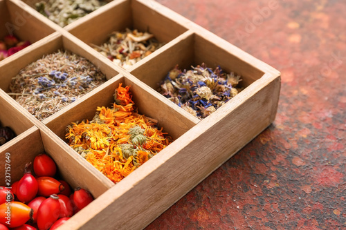 Wooden box with various dried flowers, herbs and rose hips on color table © Pixel-Shot