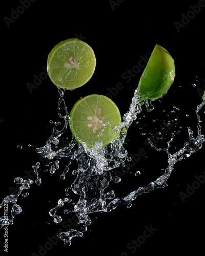 Limes with water splash or explosion flying in the air isolated on black background