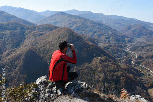 Young man with a binocular on top of the hill looks in a valley. Man in nature, concept of healthy life and traveling