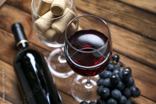 Glasses of red wine and corks on wooden table