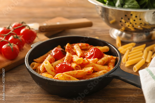 Frying pan with tasty penne pasta on wooden table