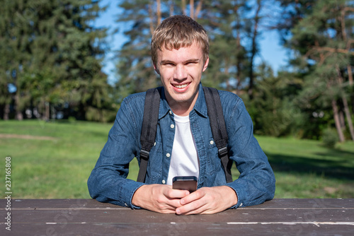 Happy teenager sitting at a picnic table while using his cell phone. © Brian
