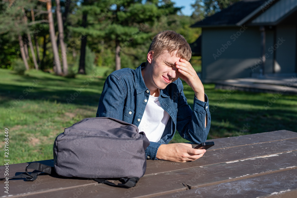 Concerned teenager sitting at a picnic table all alone with his phone. Concerned teenager sitting at a picnic table all alone with his phone.