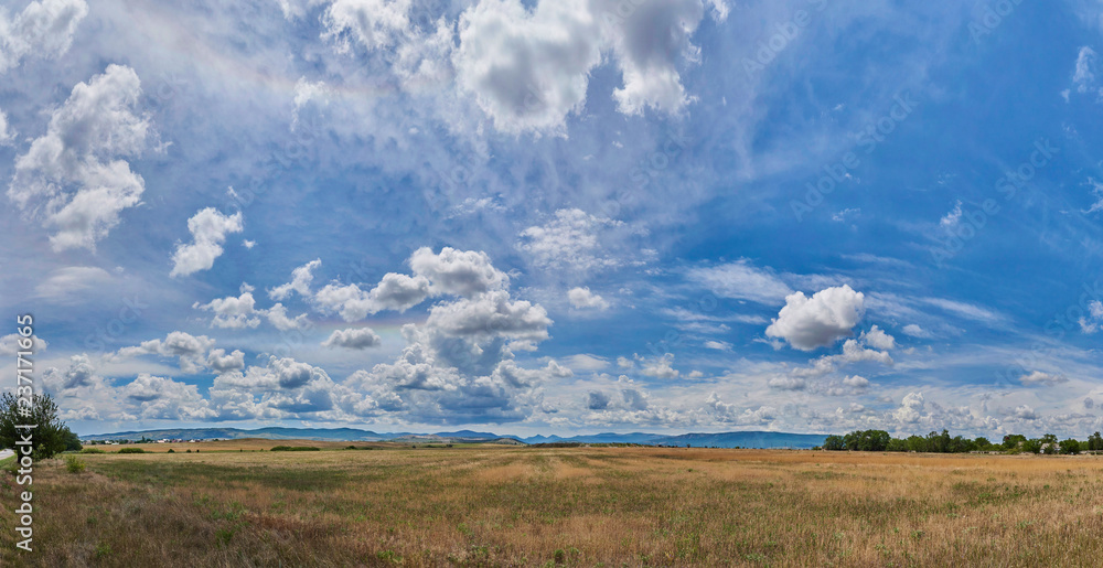 Panorama of a beautiful cloudy sky over the fields against the backdrop of mountains.