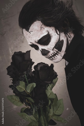 Skull face makyup guy holding black roses.