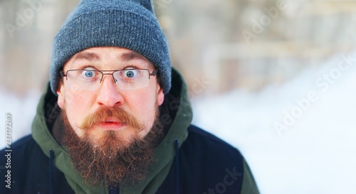 Young bearded guy with glasses and warm winter clothes in shock