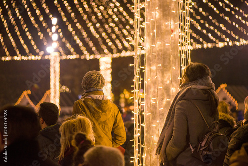 Christmas market and concert in city centre. People enjoying event, taking pictures and videos. Beautiful decorations and glowing lights. 