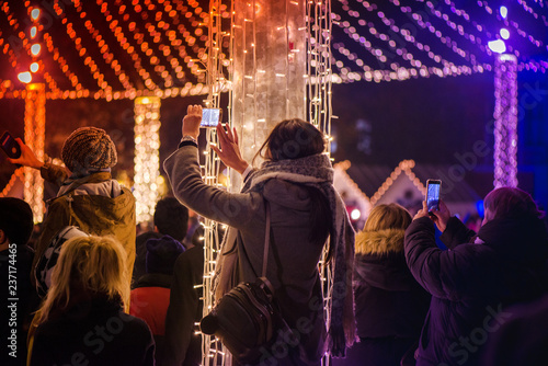 Christmas market and concert in city centre. People enjoying event, taking pictures and videos. Beautiful decorations and glowing lights.  