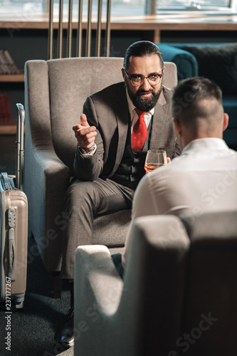 Bearded man sitting on armchair near his luggage in hotel lobby