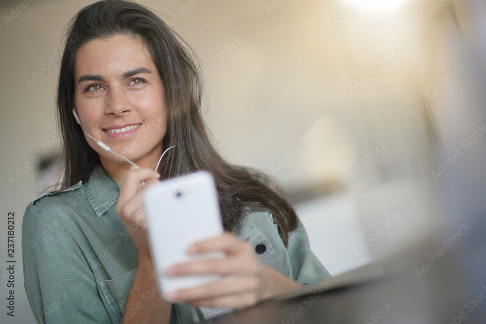 Beautiful brunette talking on cellphone with headphones at home Beautiful brunette talking on cellphone with headphones at home