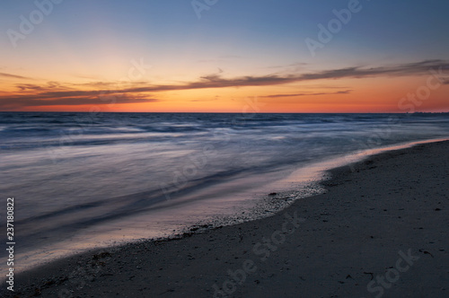 Yellow, orange and blue colors in twilight after sunset illuminate the sky and shiny, silky water along Barefoot Beach, Florida at twilight.