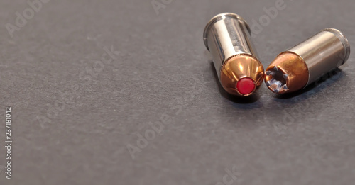 A 40 caliber hollow point bullet and a 44spl red tipped bullet laying together on a gray background with room for text