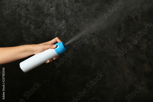 Woman spraying air freshener on dark background