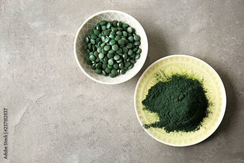 Plates with spirulina tablets and powder on grey table