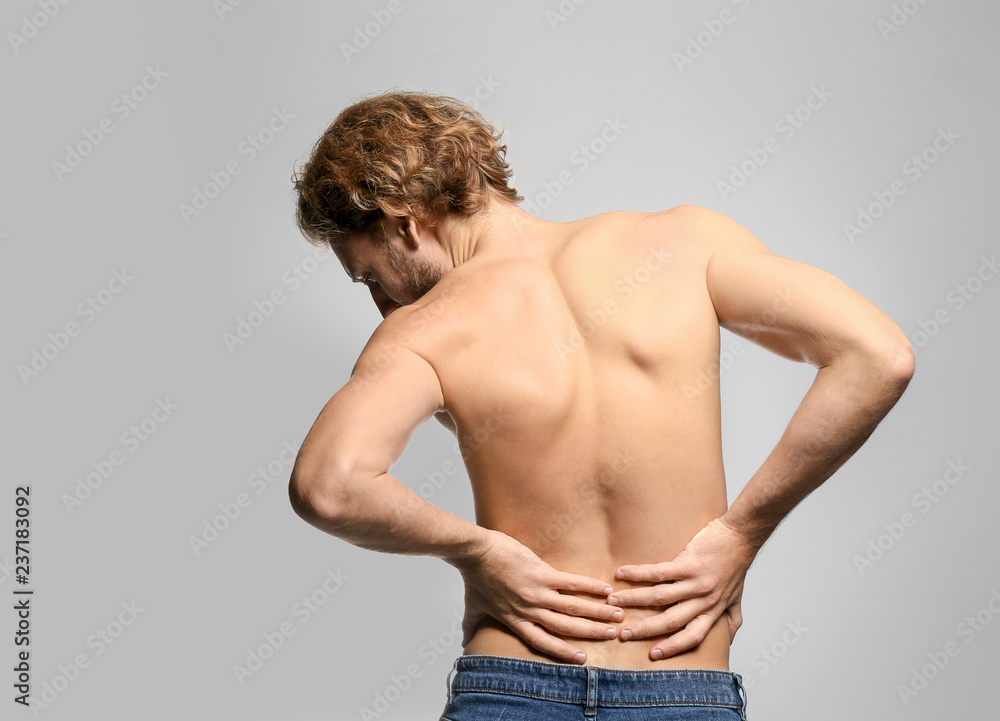 Young man suffering from back pain on light background Young man suffering from back pain on light background