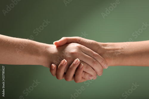 Young people shaking hands on color background