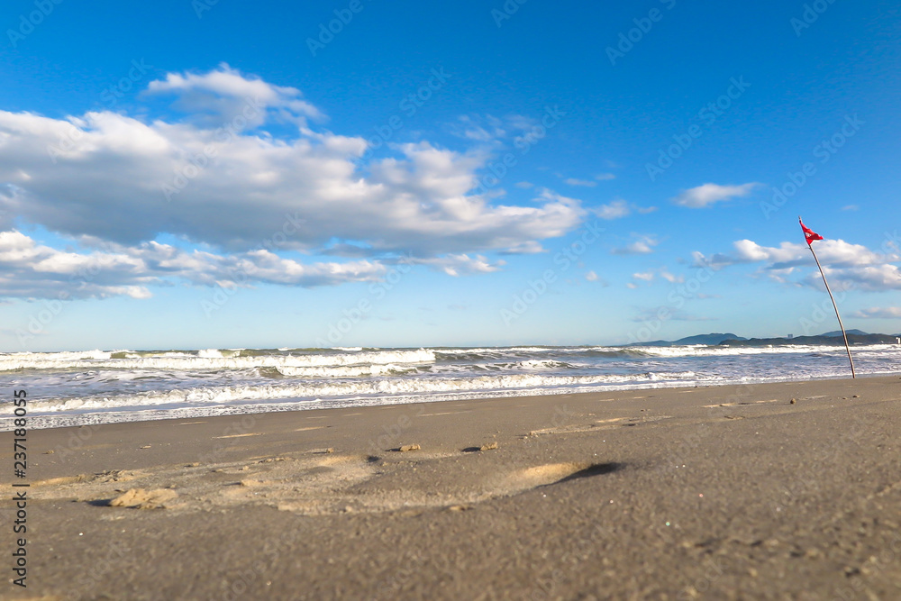Navegantes beach in the late afternoon, with red flag and rough sea, blue sky with clouds, Navegantes, Santa Catarina