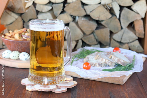 Mug of light beer and snack on the table against the background of firewood.