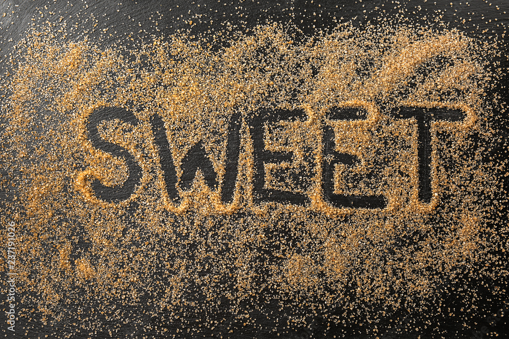 Inscription SWEET with granulated cane sugar on dark table