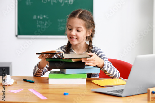 Photos Cute girl with stack of books sitting in classroom