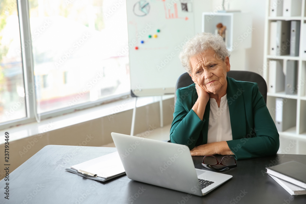 Senior woman suffering from neck pain while sitting at table with laptop Senior woman suffering from neck pain while sitting at table with laptop