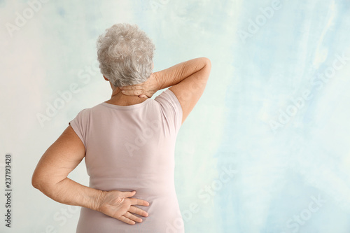 Senior woman suffering from back pain on light background