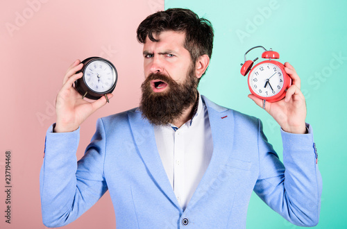 Guy unshaven puzzled face having problems with changing time. Time zone. Does changing clock mess with your health. Man bearded hipster hold two different clocks. Changing time zones affect health