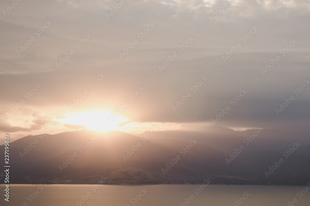 abstract unfocused mountain silhouette shape with sun rise light and glares from behind ridge with soft colors in morning time, nature wallpaper calendar concept
