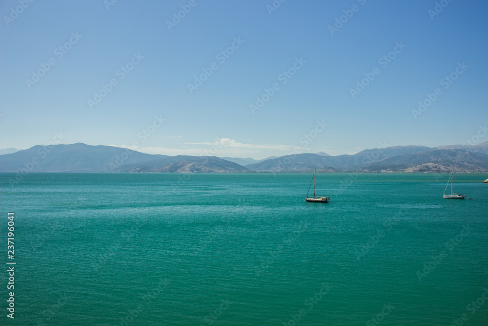 Mediterranean landscape and seascape with ships and boats on vivid green and blue water surface and mountain ridge shape on horizon background, copy space