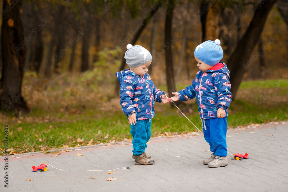 Twins are playing with toy airplanes in the autumn park Twins are playing with toy airplanes in the autumn park