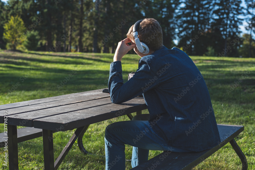 Fototapeta premium Concerned teenager listening to music with his headphones while sitting alone at a picnic table.