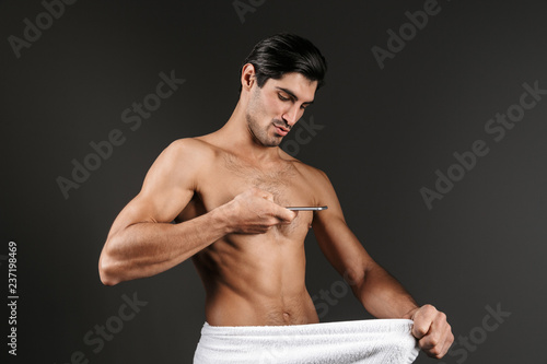 Naked man isolated over dark background covering his genitals with towel take an intimate photo by mobile phone. photo