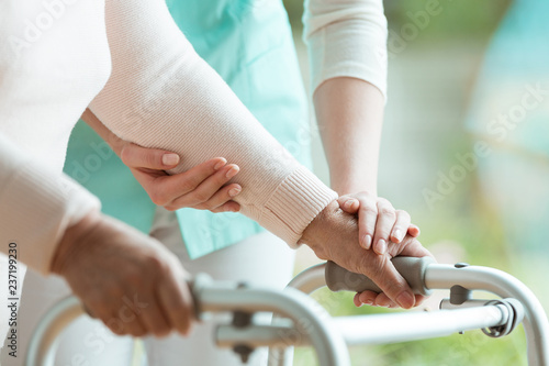 Closeup of senior lady's hands holding a walker and helpful nurse supporting her