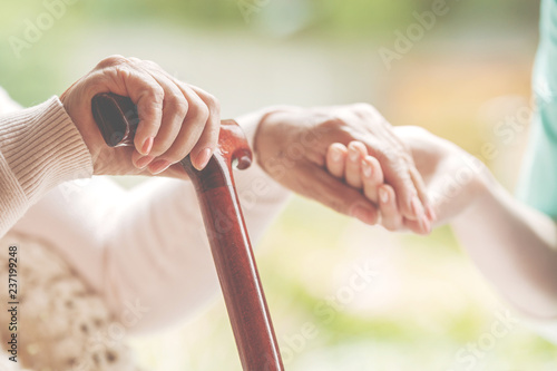 Closeup of senior lady holding walking stick in one hand and holding nurse's hand in the other